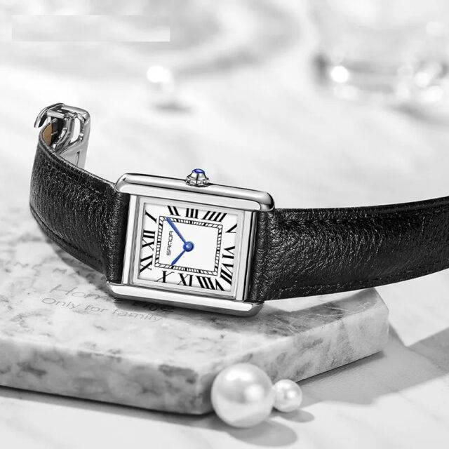 Luxury watch with black leather strap on a marble surface with pearls