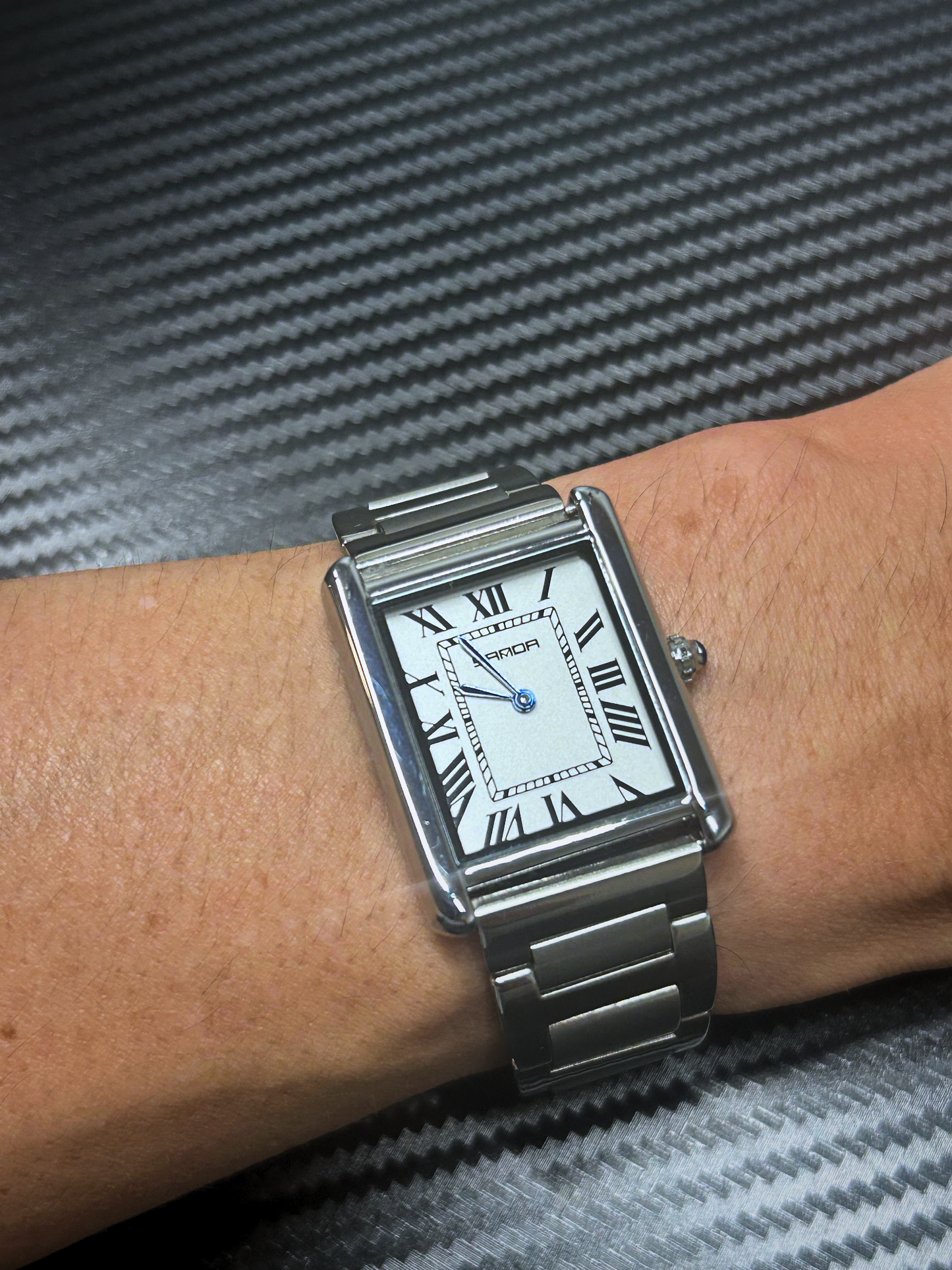 Silver wristwatch with a white face featuring Roman numerals on a person's wrist.