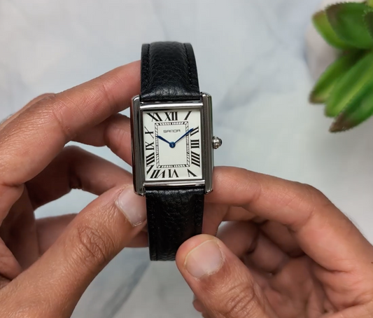 Person holding a black square wristwatch with a white face