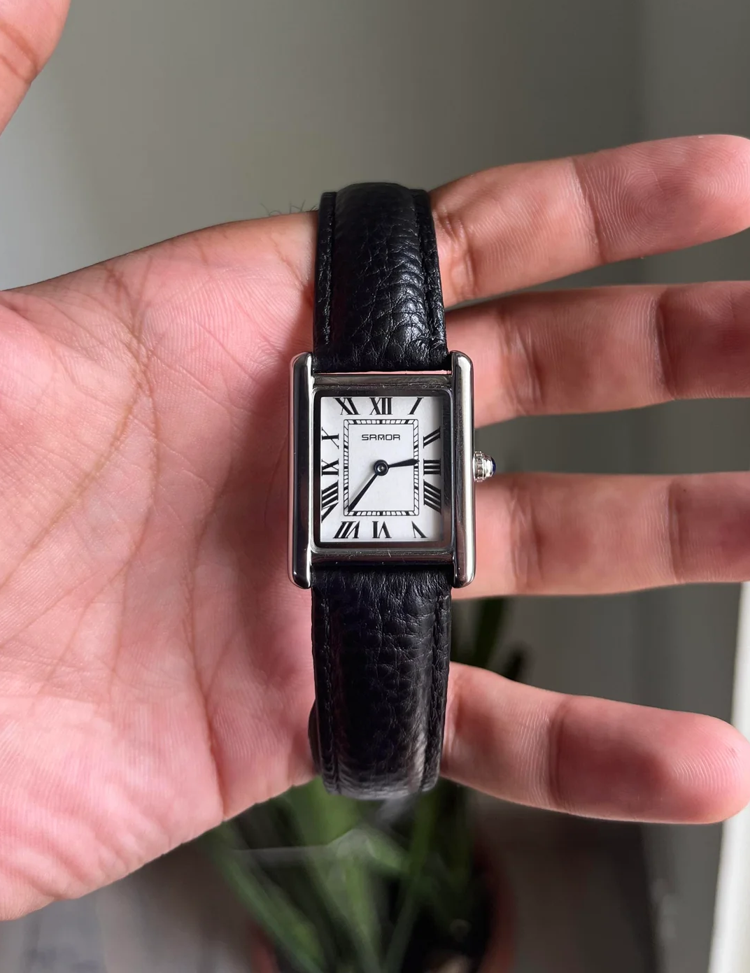 Black wristwatch with a silver case on a person's wrist against a neutral background. Sanda 1108 black leather strap